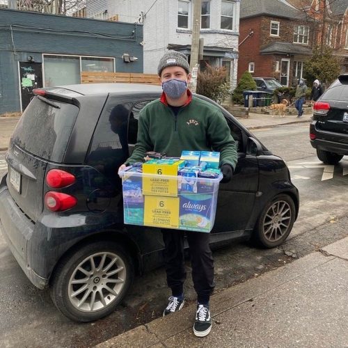 Hanlon holding a container or menstrual products in front of his car