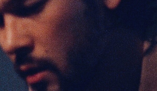 Justin Nozuka looking downwards in a dimly lit room.