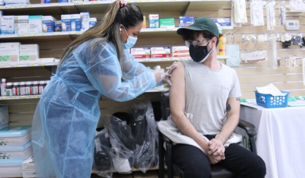A person is sitting down while a person standing gives them a needle shot inside a clinic