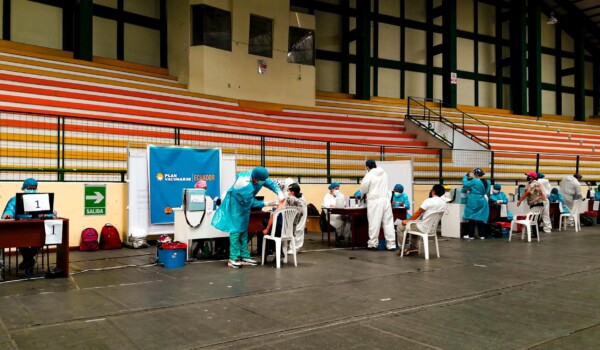 A roll of people sitting down in an arena to receive a needle from a nurse