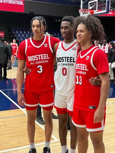 Three people in red and white basketball uniforms are standing together on a wooden court indoors.