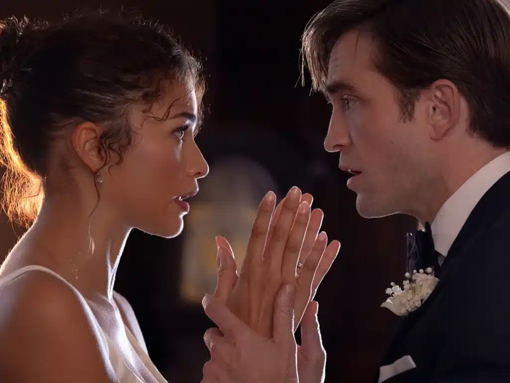 Image from the side of Charlie (Robert Pattinson) holding Emma (Zendaya) by the wrists while they look directly in eachother's eyes, dressed in wedding attire.